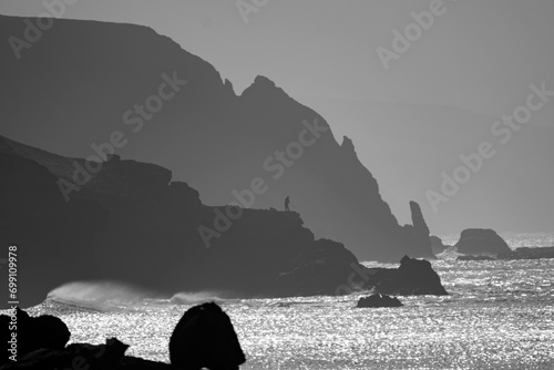 View of the silhouettes of rocks, the ocean and the figure of a fisherman in the distance on the beach La Pared on the Canary island of Fuerteventura, Spain.