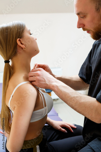 A male physiotherapist is massaging the neck of a relaxed woman sitting on a stretcher. He uses kinesio tape. Body taping