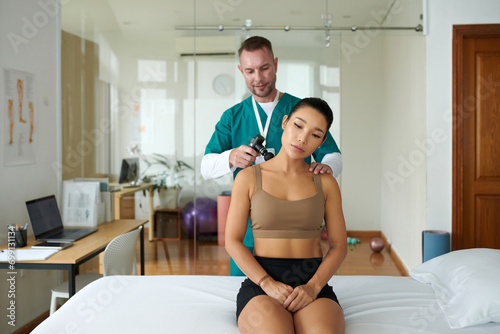 Therapist using massage gun when working with patient in his office