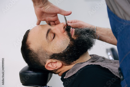 Man shaving his beard with razor in the barbershop