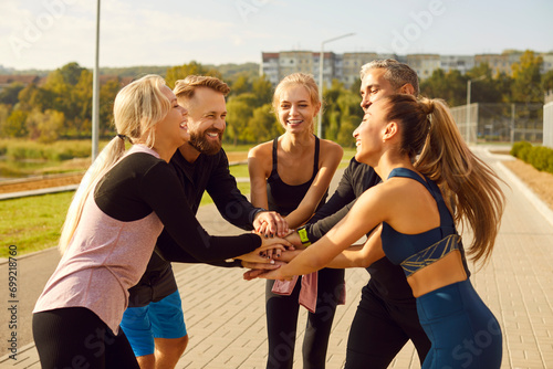 Happy smiling sporty group of people standing in a circle with hands in stack in the morning after sport training in the city park. Workout in nature and healthy lifestyle concept.