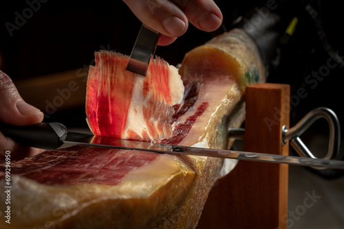 Close up of gourmet cutter slicing acorn fed iberian ham. Spanish delicatessen food.