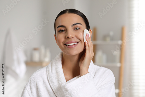 Beautiful woman removing makeup with cotton pad in bathroom