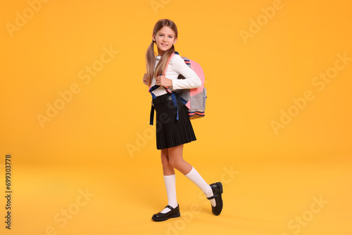 Happy schoolgirl with backpack on orange background