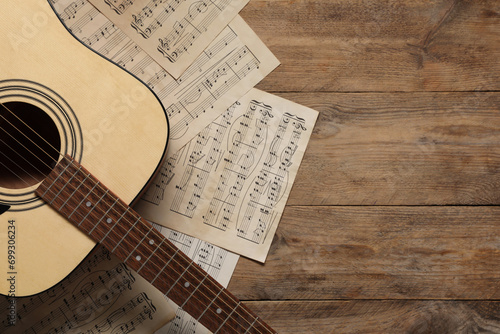 Paper sheets with music notes and acoustic guitar on wooden table, top view. Space for text