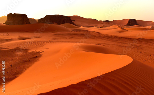 Sahara desert, orange dunes. Holidays and travel in Algeria, morning light over the desert. Rocks in the background. Fine lines of sand dunes.