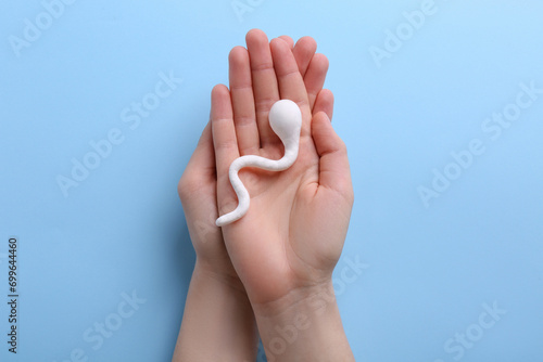 Reproductive medicine. Woman holding figure of sperm cell on light blue background, top view