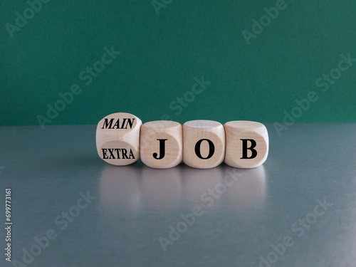 Extra or main job symbol. Turned a wooden cube and changes concept words Extra job to Main job. Beautiful green background, grey table, copy space. Business extra or main job concept.