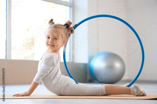 Cute little girl doing gymnastics with hula hoop on mat in gym