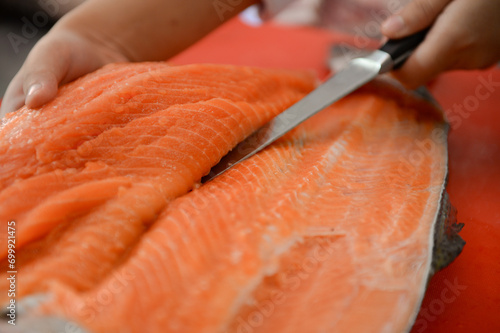 Fresh salmon fillet close-up on white cutting board table while filleting salmon belly by chef in cooking room