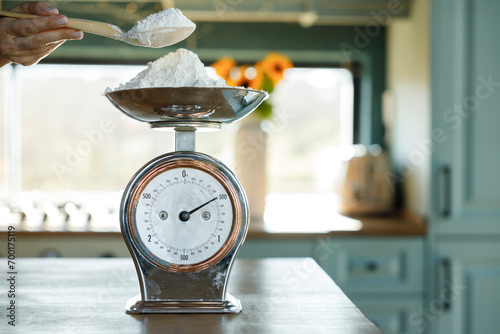Woman's hand putting flour on an antique scale on the kitchen counter