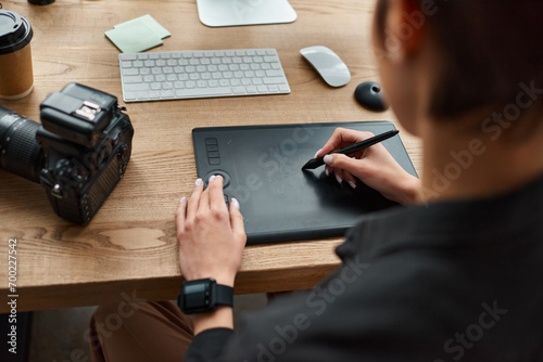 cropped view of young female designer sitting at desk and using modern drawing tablet for work