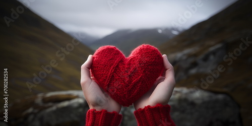 Red heart in hands against a mountain landscape. Love of nature, Valentine's Day, travel and adventure concept.