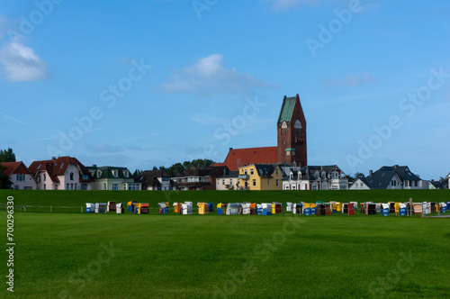 Parish Church of Saint Peter (St. Petri) in background, it was garrison church, built in 1911. Unused hooded beach chairs (strandkorb) on green grass field. Cuxhaven, Germany.