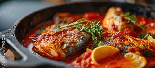 Modern design cast-iron roasting dish showcases closeup of moqueca baiana fish stew with fish in tomato sauce.