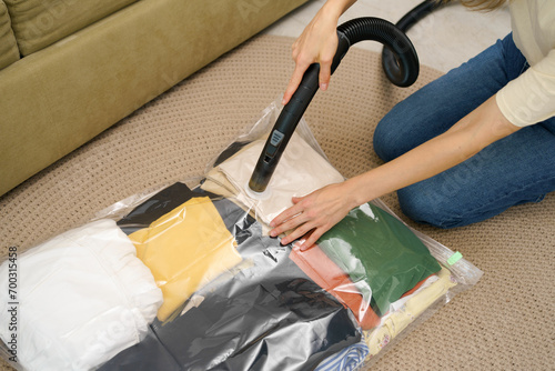 A young woman uses a vacuum cleaner to extract air from a vacuum bag with clothes for compact storage in a closet while sitting on the floor. Space saving concept, compressed packaging and seal bag