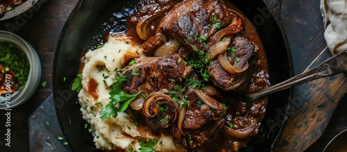 Contemporary slow-cooked lamb in red wine sauce with shallots and mashed potatoes seen from above on a cast iron plate