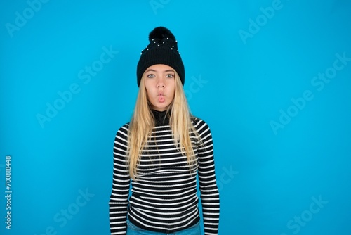 Teen caucasian girl wearing striped sweater and woolly hat making fish face with lips, crazy and comical gesture. Funny expression.