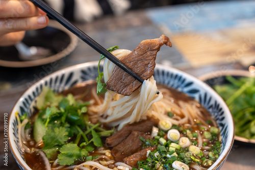 Closeup photo of beef rice noodle (pho) held in chopsticks, taken in a restaurant