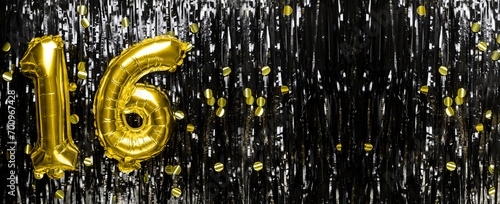 Gold foil balloon number number 16 on a background of black tinsel decoration. Birthday greeting card, inscription sixteen. Anniversary event. Banner.