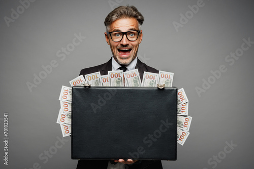 Adult rich happy employee business man corporate lawyer he wears classic formal black suit shirt tie work in office hold of cash money in case for dollar banknotes isolated on plain grey background.