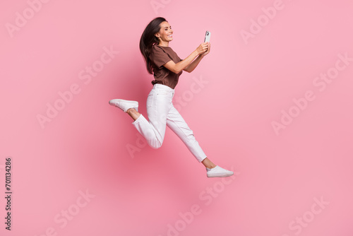 Full body length photo of young active blogging lady running in air with phone sending video message isolated on pink color background