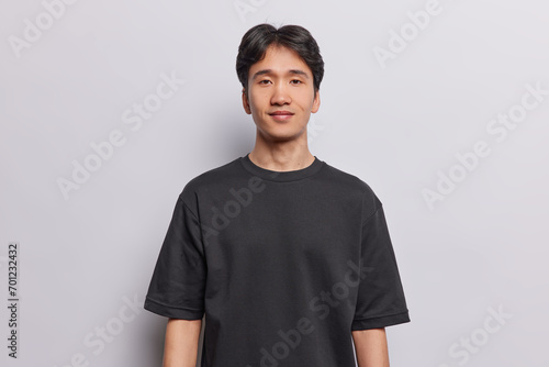 Portrait of handsome brunet adult Japanese man wears casual t shirt focused at camera has pleased expression looks directly at camera isolated over white background. People and emotions concept