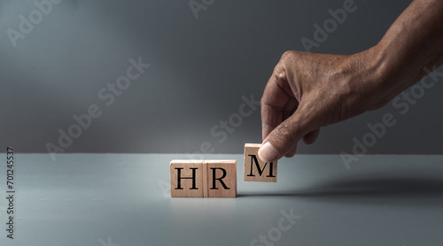 hand posing wooden blocks with HRM or human resources management , concept of human resources , leadership and discrimination. grey blue background , copy space .