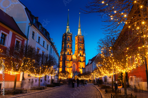 Street with cobblestone road, lights on trees, St. John the Baptist Cathedral with two spiers in the old historical city center, Tumski Island, Wroclaw, Poland