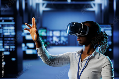 Computer scientist in data center uses virtual reality to prevent system overload. African american VR headset user in server room ensuring enough network bandwidth for smooth operations