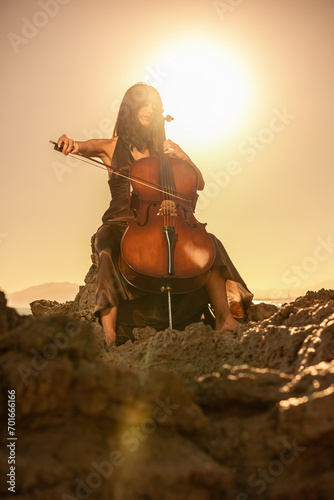 Woman playing cello in nature with sunset sunlight behind her