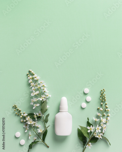 Seasonal allergy concept, spring blooming branches tree and mock up nasal spray white bottle, pills on green background, top view, flat lay. Healthy lifestyle, treatment seasonal allergies
