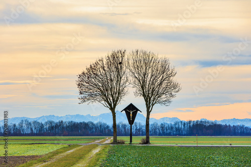 a field path near Graben near Augsburg leads to a wayside cross under a cloudy sky with the Alps in the background