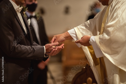 Ein Pfarrer reicht dem Bräutigam während der Trauung eine Hostie.