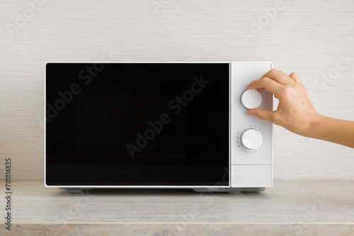 Young adult woman hand rotating white button of dark black microwave oven and setting temperature or functions for food warming on table top at home kitchen. Closeup. Front view.