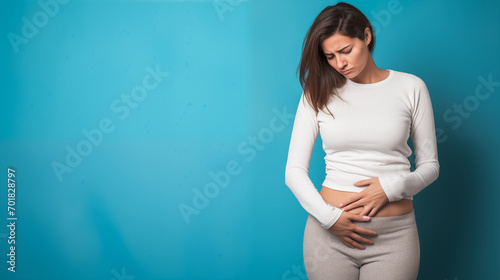 A young woman doubled over in discomfort against a blue backdrop.