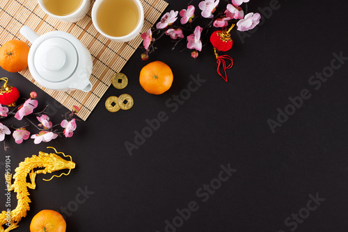 Elevating celebrations through the chinese New Year tea ceremony. Top view shot of teapot, cups of tea, gold dragon, mandarins, traditional chinese elements on black background with promo zone