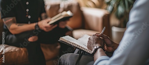 A shrink is interviewing his client and writing down notes in a textbook during a session A psychoanalyst is asking questions and writing down notes while a client is sitting on the therapist s