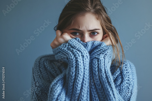 Woman in blue turtleneck knitted sweater sadly looking at camera while covering sad face. Feelings of depression, sadness, loneliness, social phobia. Winter cold. Blue Monday
