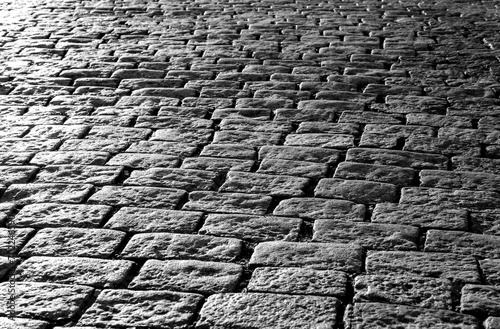 Old cobblestones on a historic square near the castle of Tübingen, Germany. Shiny basalt ashlars and blocks reflecting sunshine. Pavement background, black and white greyscale with high contrast.