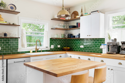 A kitchen detail with butcher block wood countertops, white cabinets, a gold fixture hanging over the island, and green subway tile backsplash. No brands or logos.