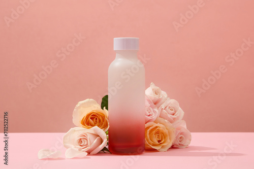 An unlabeled bottle is placed in the center of the frame with fresh roses on a pink background. With natural astringent essence, rose water helps shrink pores and brighten skin.