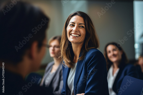 A woman in a group smiling at a woman meeting at a conference room, in the style of artistic reportage, back button focus, light amber and indigo, viennese actionism, focus on joints/connections, shap