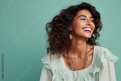 A smiling young model wearing a boho-chic maxi dress, accessorized with statement jewelry, against a solid light mint green background.
