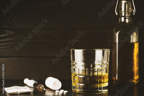 Alcohol drink in a glass, white pills, syringe with drug substance, heroin dose, narcotics powder in transparent bag on wooden table. Concept of addiction and bad habits