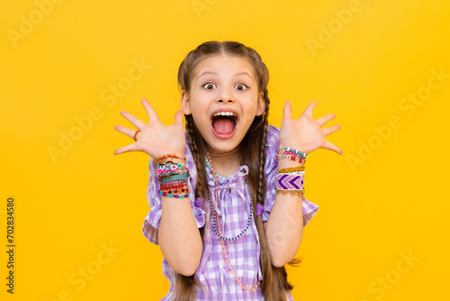 The happy little girl opened her mouth wide with delight and spread her fingers in different directions. The child dressed up in colorful beaded bracelets. Beading for children and teenagers.