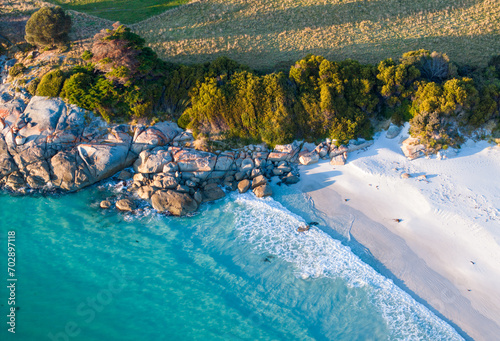 Aerial shot of a beautiful beach with turquoise waters, green trees, and rocks