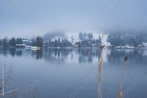 Idyllically located houses on Lake Walchsee in Tyrol, Austria. View of water. Reflection in the water, snow-covered landscape, mountains shrouded in fog