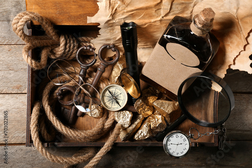 Box with travel equipment, golden nuggets and bottle of rum on brown wooden background