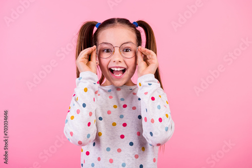 Photo of impressed small girl with tails hairstyle wear stylish sweatshirt touching glasses staring isolated on pink color background